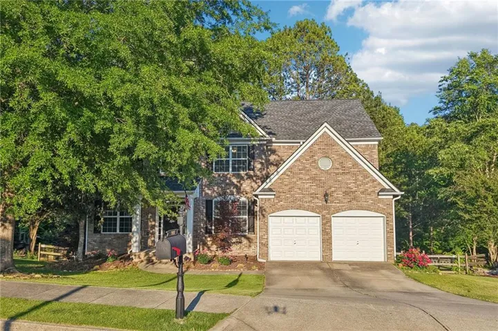Brick-front residence featuring a two-car garage, pitched roofline, and mature landscaping