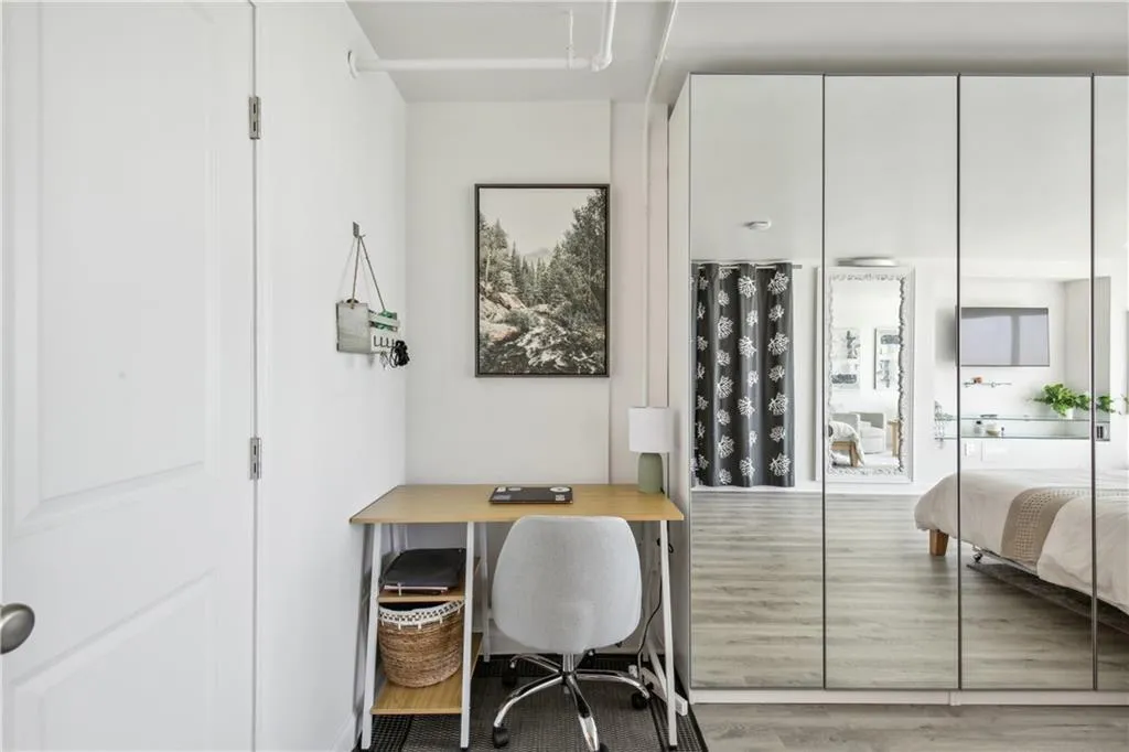 Mirrored closet doors, light wood-finish flooring, white walls, and a recessed desk area
