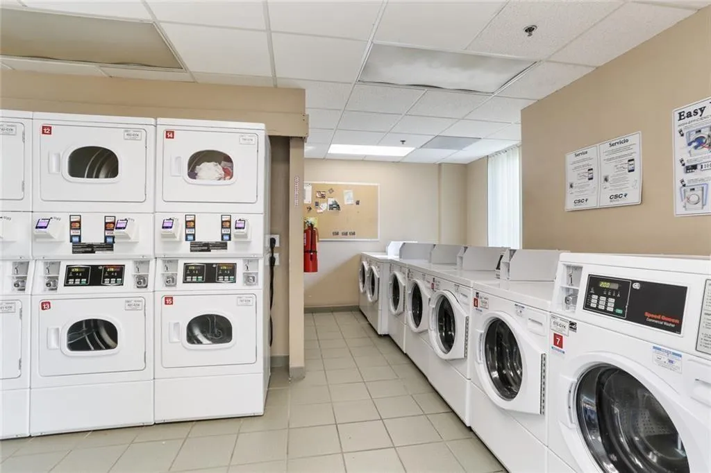 On-site laundry facility featuring multiple front-loading washers and dryers, tile flooring, and neutral painted walls