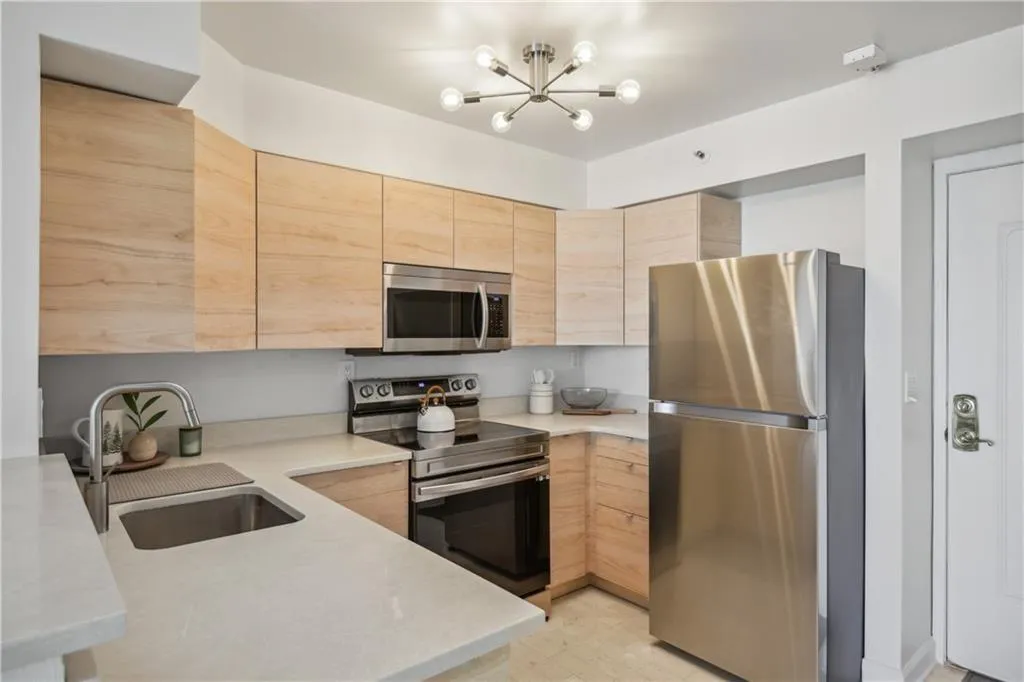 Modern kitchen featuring light wood cabinetry, stainless steel appliances including a gas range and over-the-range microwave, quartz countertops, and a undermount sink