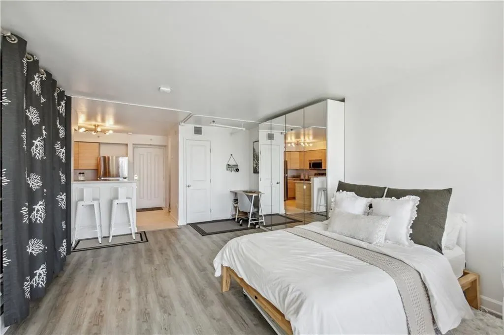 Wood-finish flooring throughout, integrated kitchen with light wood cabinetry, built-in breakfast bar, and mirrored closet doors