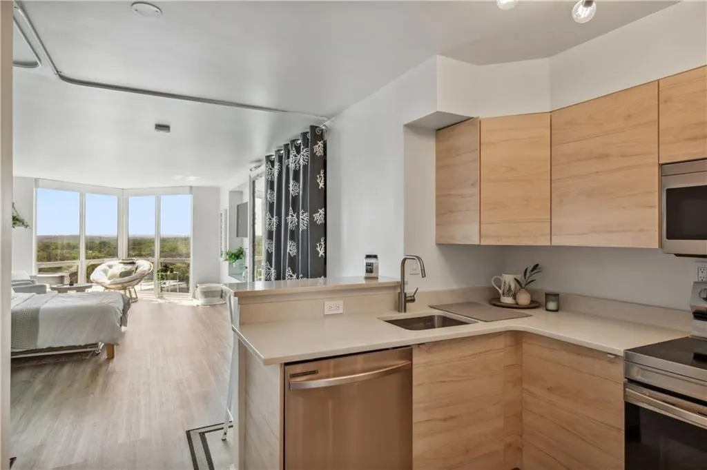 Contemporary kitchen with light wood-finish cabinetry, stainless steel appliances, and solid surface countertops