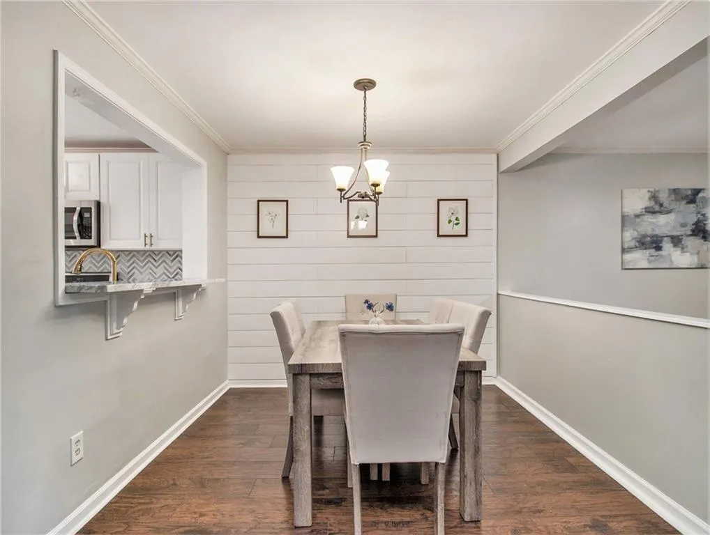 Wood-finish flooring with crown molding, white shiplap accent wall, and a pass-through window with a marble-finish breakfast bar
