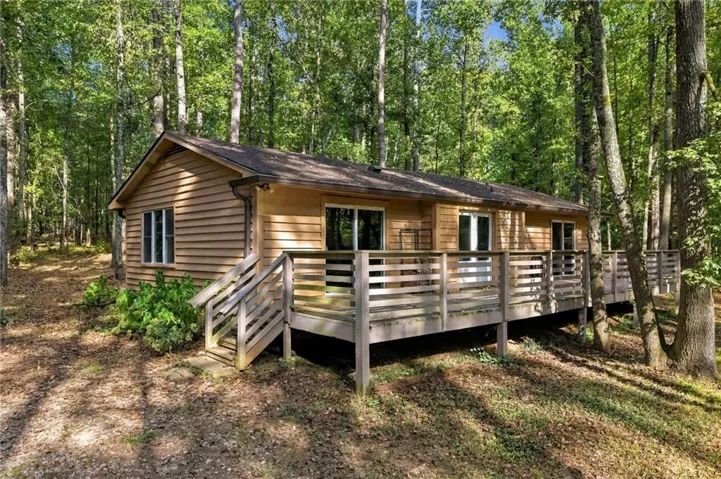 Wood-sided exterior with a natural wood deck and railing, surrounded by mature trees