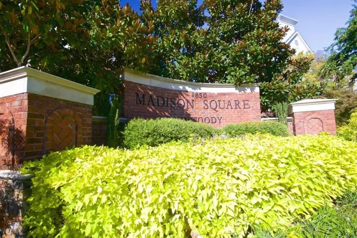 Madison Square community entrance featuring a curved brick monument sign, stone base, and mature landscaping