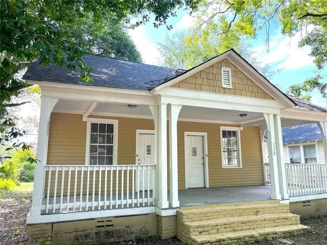 Front elevation featuring a covered porch with white columns and railings, yellow horizontal siding, and a shingled gable accent