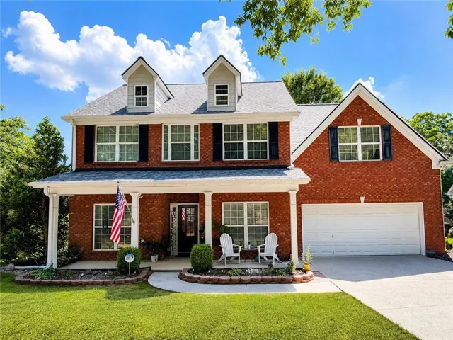 Brick exterior residence featuring a covered front porch with white columns, dormer windows, and a two-car garage with a white door