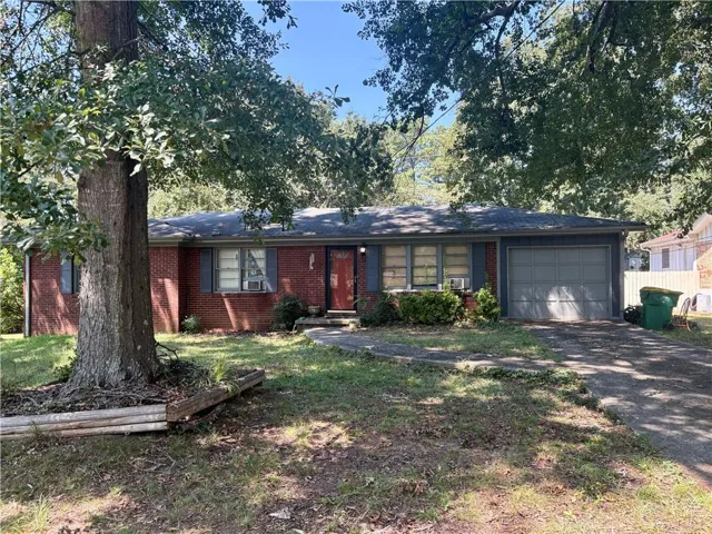 Brick exterior, attached garage, paved driveway, mature trees, and landscaping