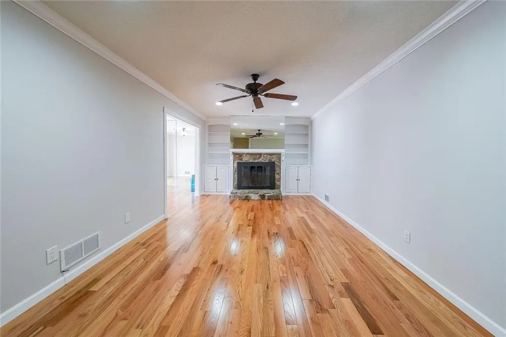Unfurnished living room featuring light hardwood / wood-style floors, ceiling fan, ornamental molding, a stone fireplace, and built in features