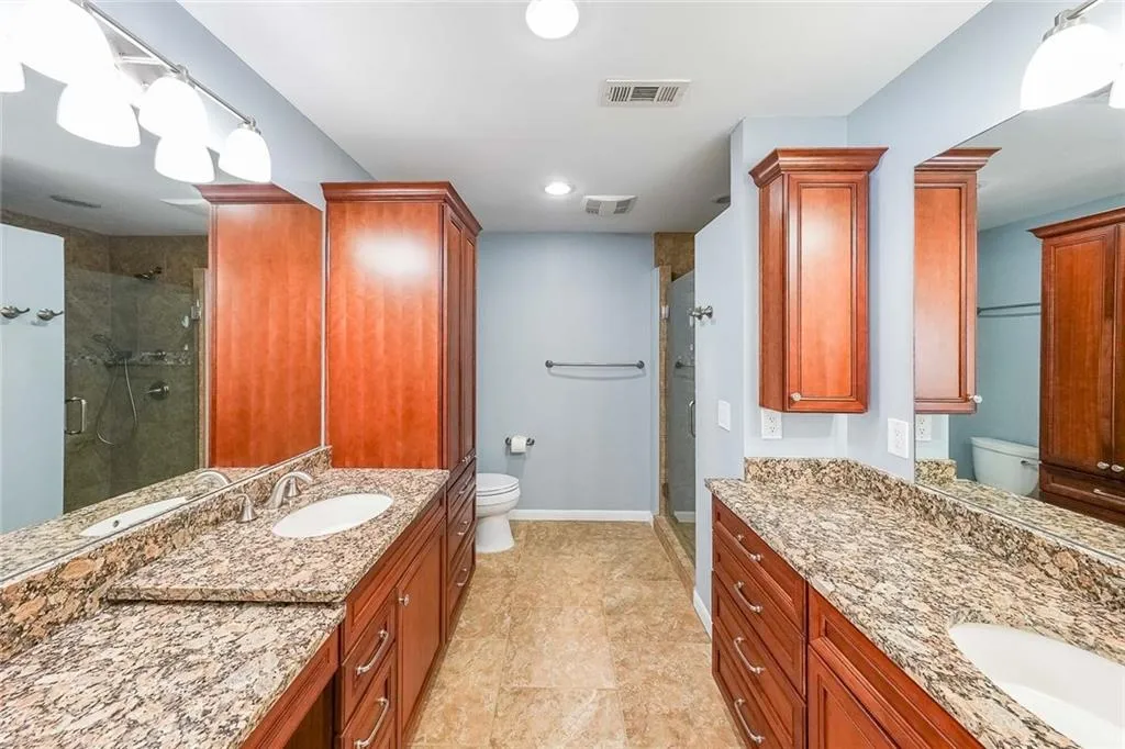 Bathroom featuring tile floors, toilet, a shower with shower door, and vanity with extensive cabinet space
