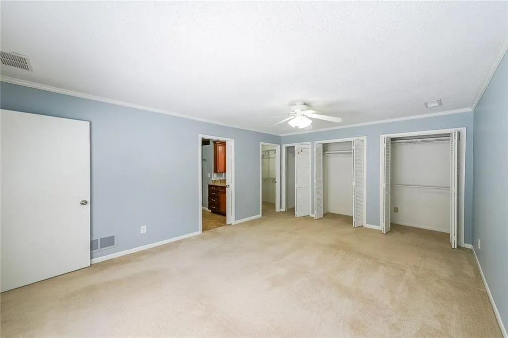Unfurnished bedroom featuring ceiling fan, ornamental molding, light carpet, ensuite bath, and multiple closets