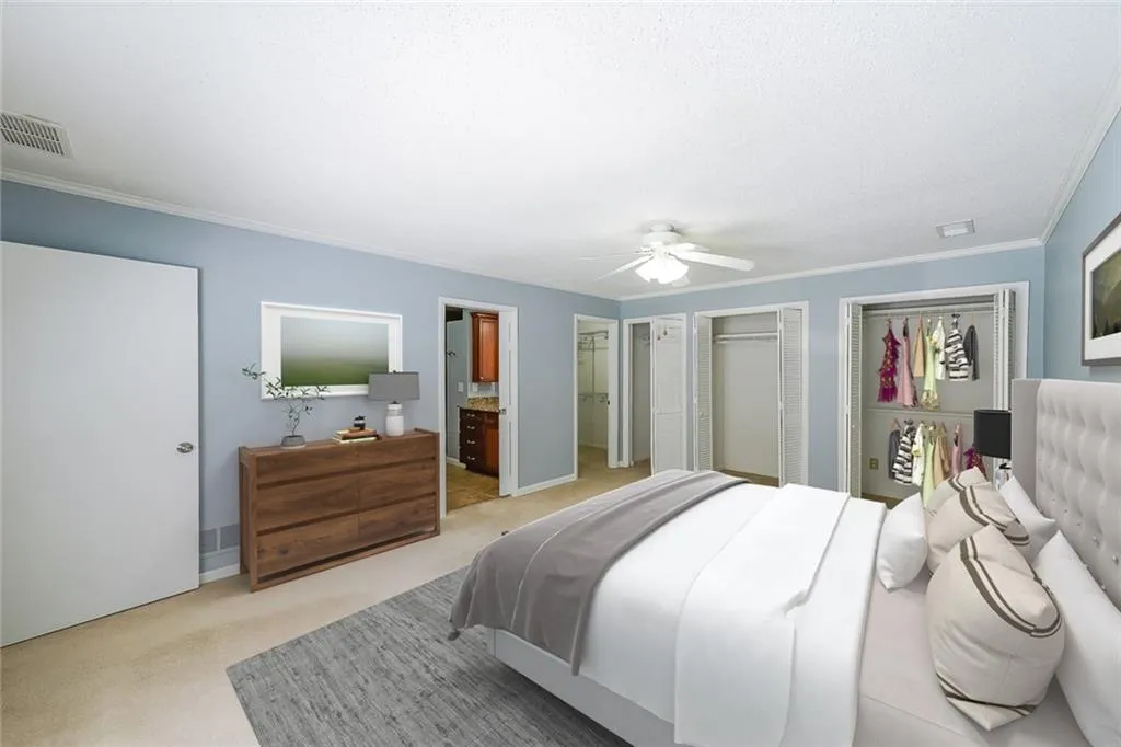 Virtually Staged Bedroom featuring ornamental molding, multiple closets, ensuite bath, carpet floors, and ceiling fan