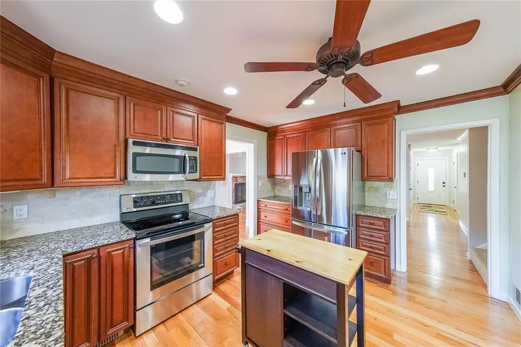 Kitchen with light wood-type flooring, light stone countertops, ceiling fan, and appliances with stainless steel finishes