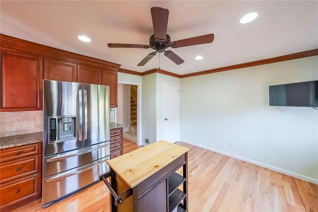 Kitchen featuring ceiling fan, stainless steel fridge, light wood-type flooring, dark stone countertops, and tasteful backsplash