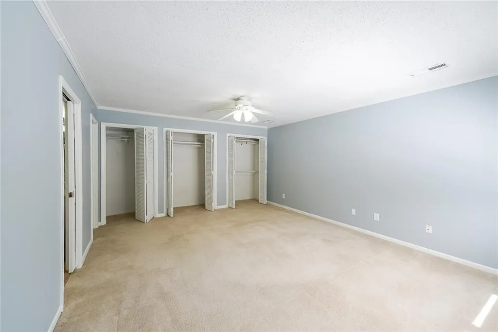 Unfurnished bedroom with crown molding, light colored carpet, ceiling fan, and multiple closets