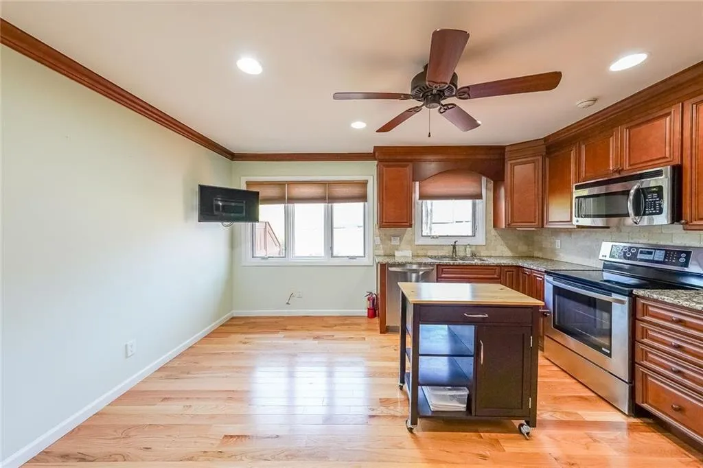 Kitchen featuring stainless steel appliances, sink, light wood-type flooring, ceiling fan, and ornamental molding