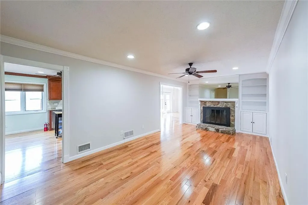 Unfurnished living room featuring crown molding, a fireplace, ceiling fan, and light wood-type flooring