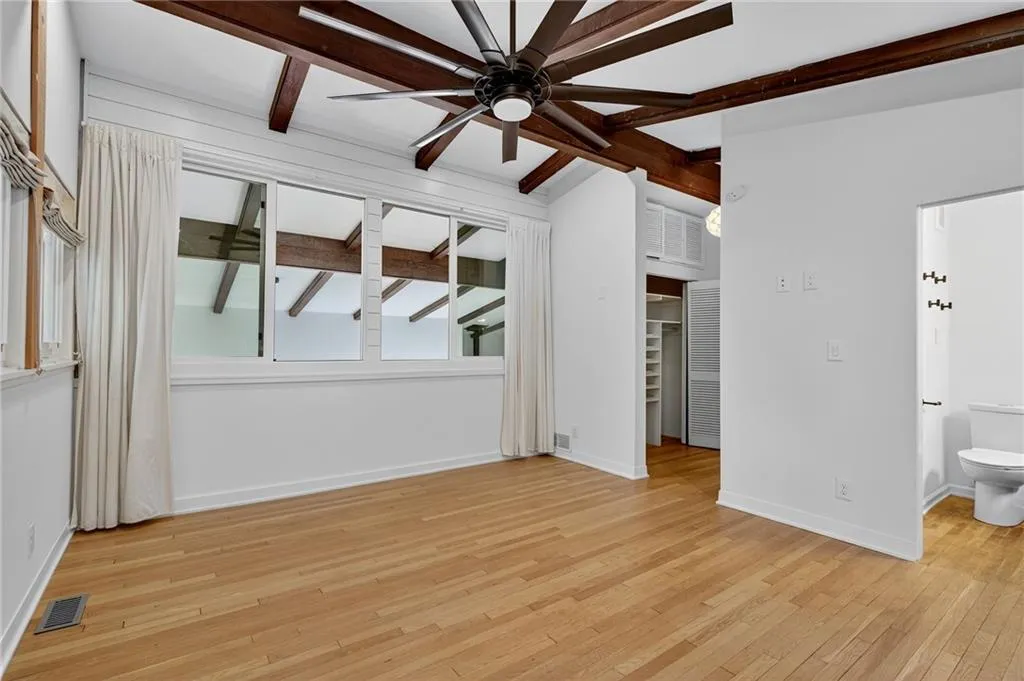Unfurnished bedroom with light wood-style flooring, ceiling fan, connected bathroom, and beam ceiling