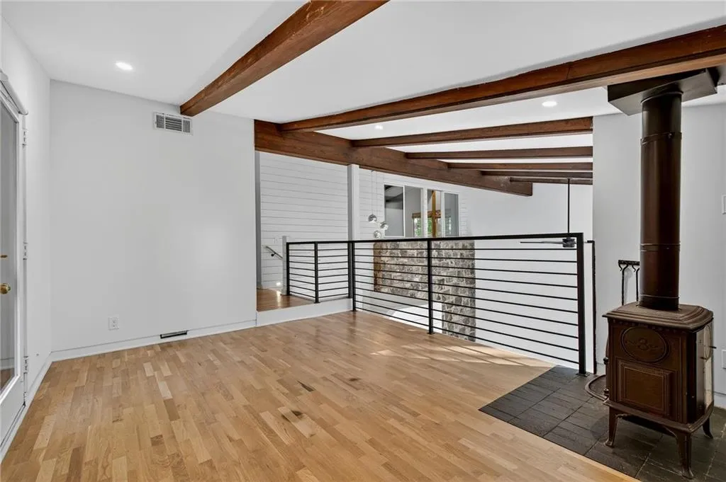 Spare room with beamed ceiling, light wood-type flooring, recessed lighting, and a wood stove