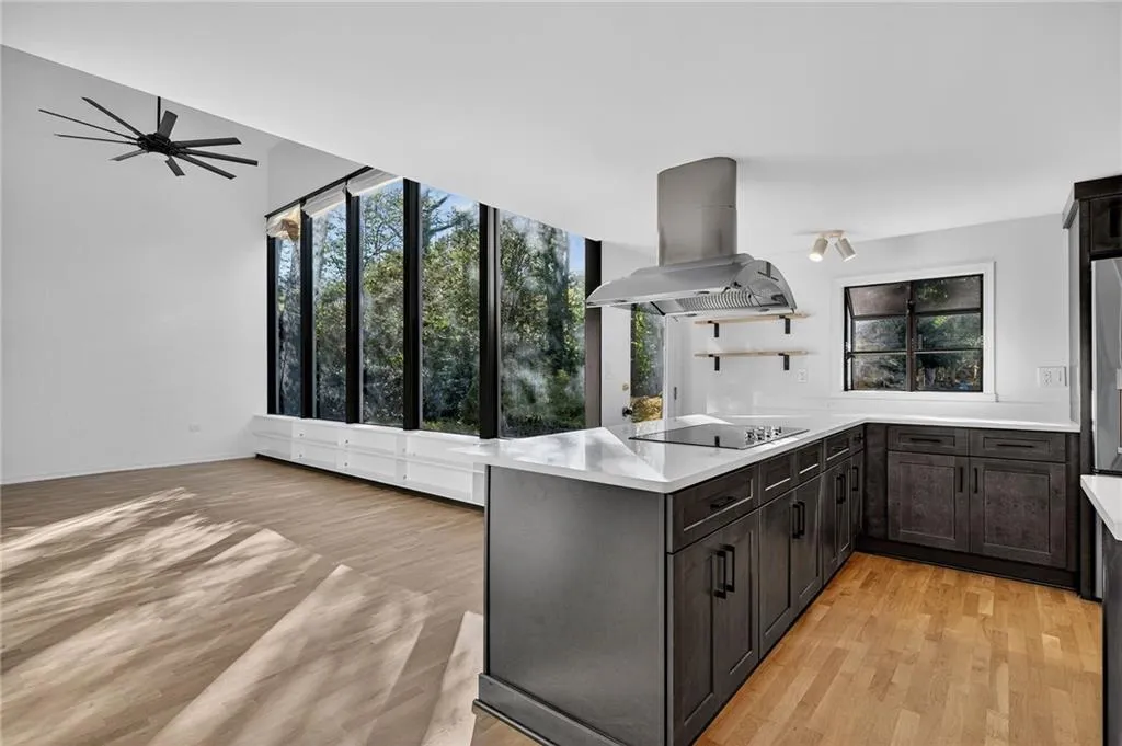 Kitchen with light wood-type flooring, a peninsula, island range hood, black electric cooktop, and light stone countertops