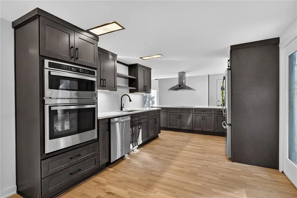 Kitchen featuring appliances with stainless steel finishes, light wood-style flooring, exhaust hood, and open shelves