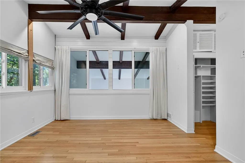 Unfurnished bedroom featuring beamed ceiling, light wood-style floors, and a ceiling fan