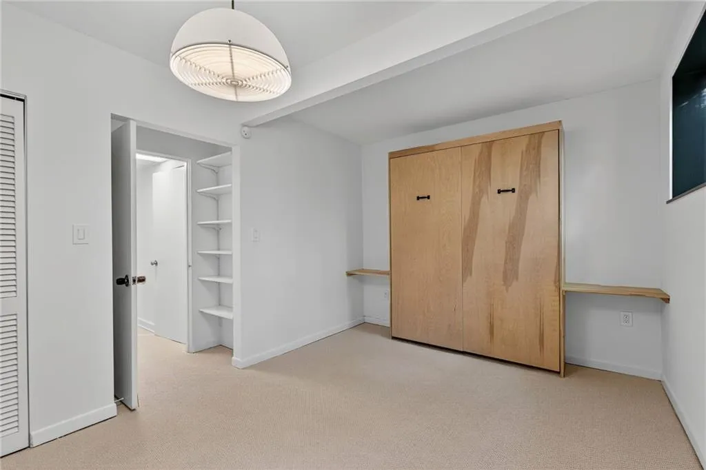 Unfurnished bedroom featuring light carpet, built in desk, and beamed ceiling