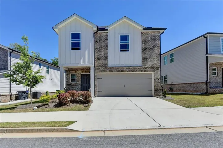 Contemporary architectural style featuring a brick and vertical siding exterior, an attached garage, a paved driveway, and established landscaping