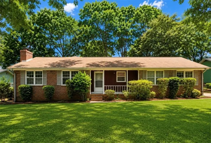 Brick exterior featuring a front porch with white railings, a red brick chimney, and a meticulously maintained front lawn
