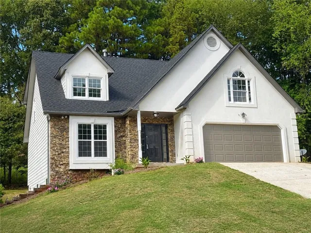 Stone and stucco exterior with a prominent front-facing garage, dormer window, arched window, and a dark entry door