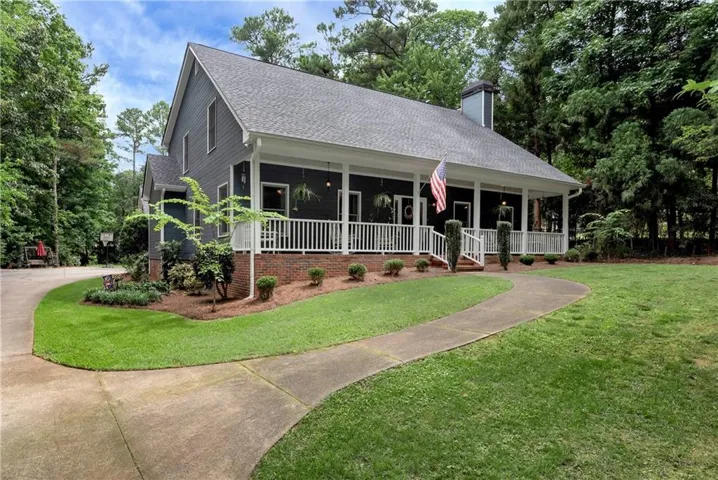 Crafted residence featuring a covered front porch with white railings, a concrete walkway, mature landscaping, a paved driveway, and a shingled roof