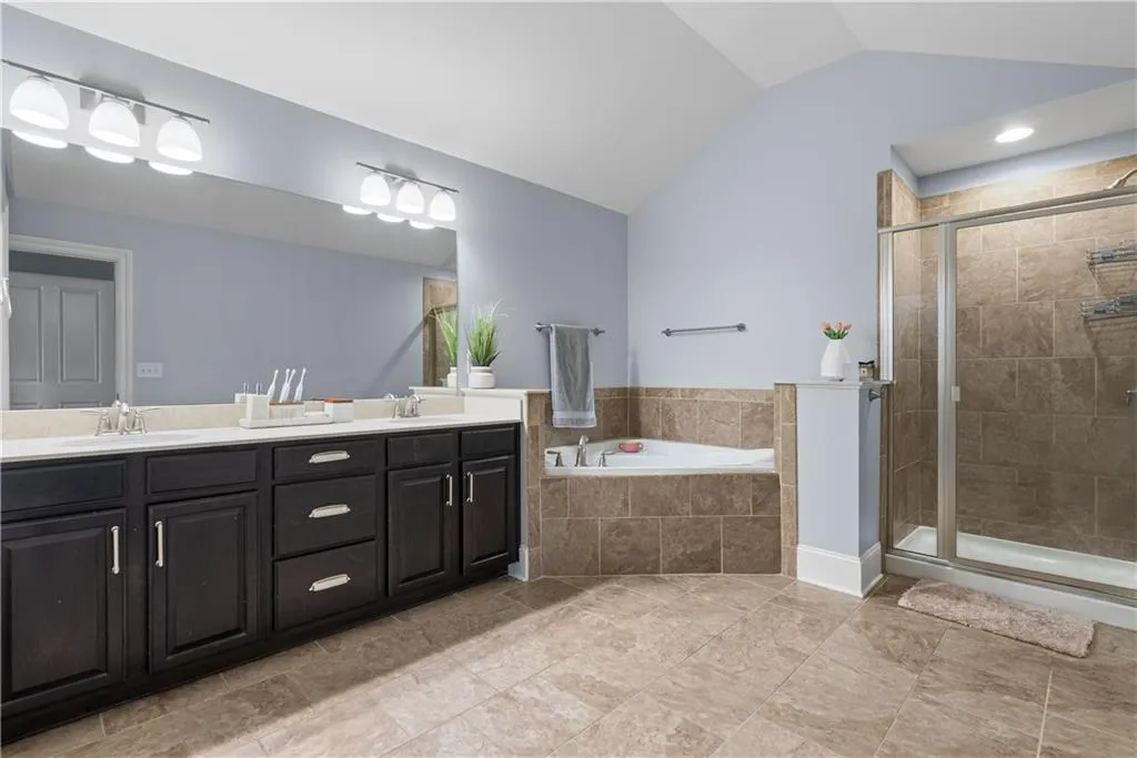Bathroom with vaulted ceiling, a shower stall, a garden tub, and a sink