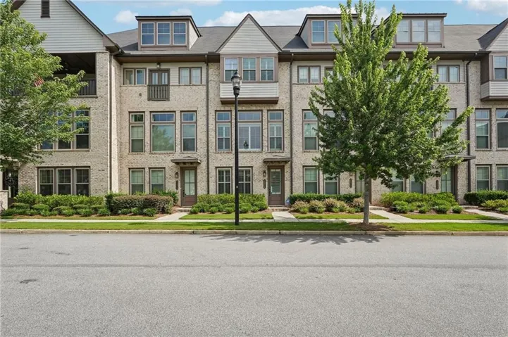 Contemporary townhouse exterior featuring light-colored brick, multiple window styles, a covered balcony, and dormer windows