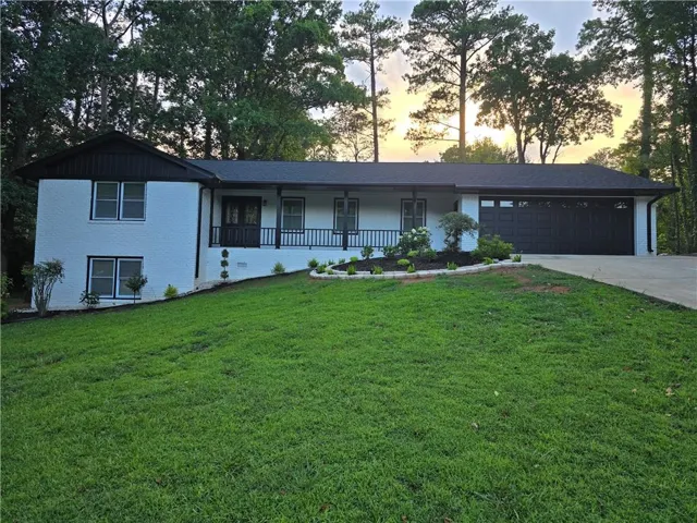 White brick exterior featuring a dark trim, an attached garage, a front porch with black railings, and a landscaped front yard