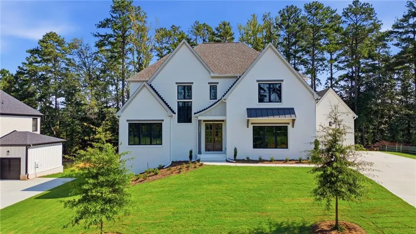 Modern farmhouse exterior with white painted brick, dark-framed windows, a covered entry, and a detached two-car garage