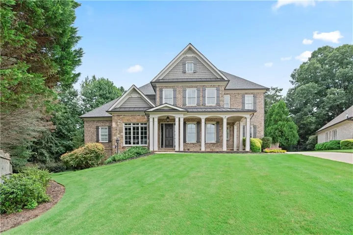 Brick and shingle exterior with a covered porch featuring columns, a gabled roofline, and dormer windows