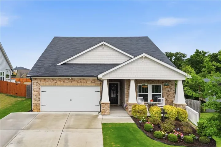 Exterior featuring brick and shingle siding, a dark asphalt shingle roof, a concrete driveway, an integrated garage, and a landscaped front yard with a covered porch