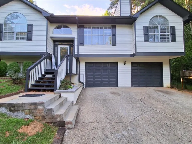 Split-level residence featuring white siding with dark trim, a two-car garage, and an elevated front entry
