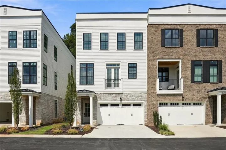 Three-story exterior featuring white horizontal siding, stone accents, black-framed windows, and an integrated two-car garage