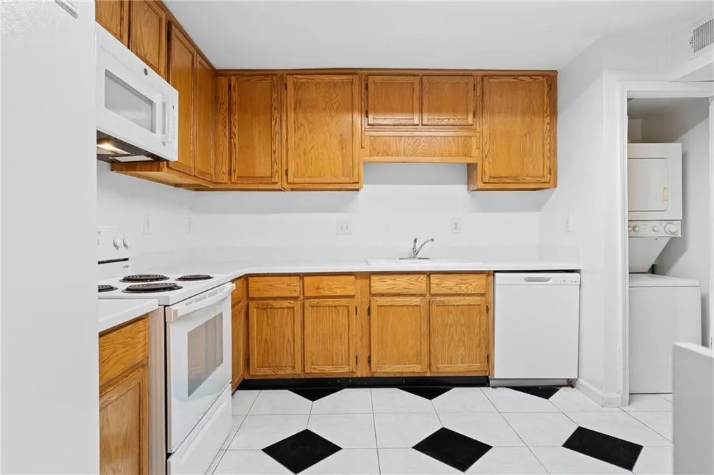Kitchen with light tile patterned floors, white appliances, stacked washer / drying machine, and sink