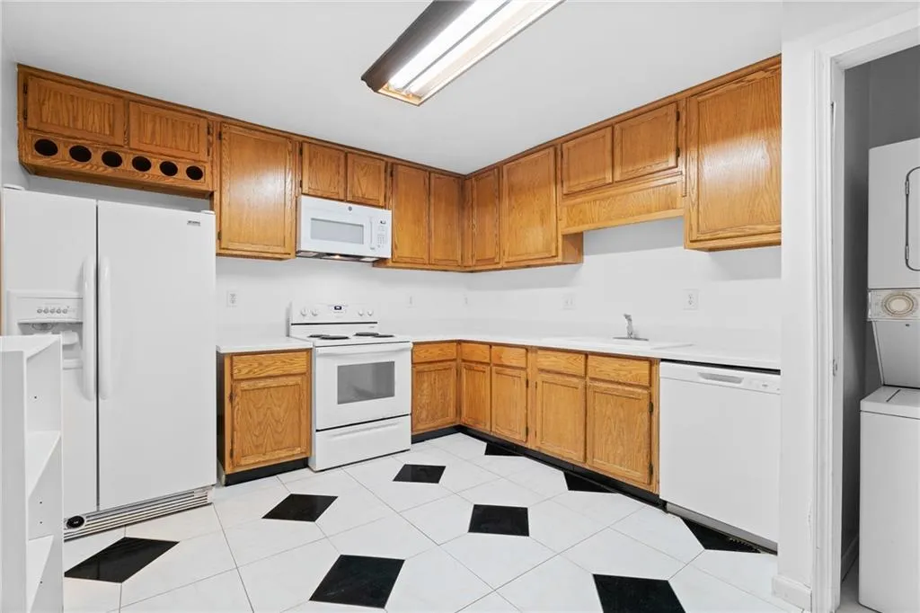 Kitchen with stacked washer / drying machine, light tile patterned floors, white appliances, and sink