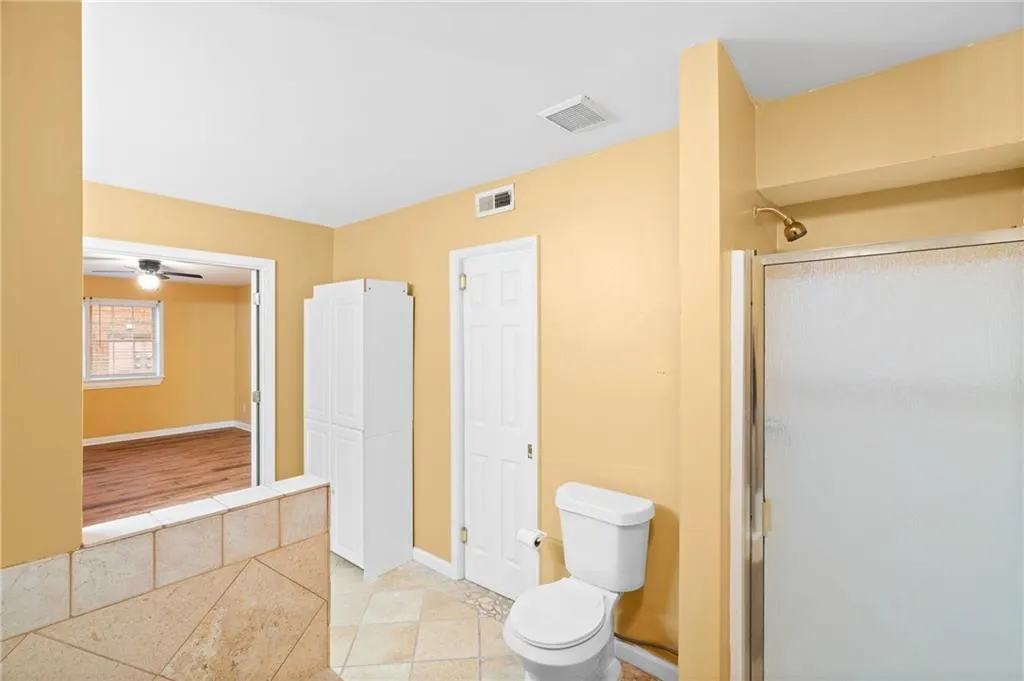 Bathroom with tile patterned flooring, toilet, a shower with door, and ceiling fan