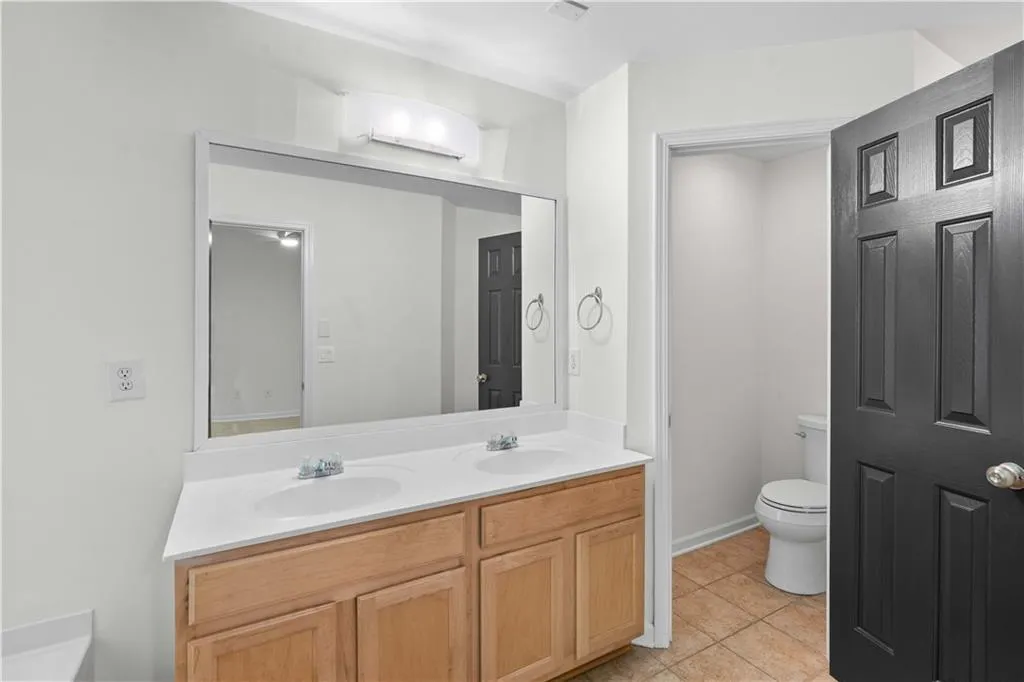 Dual vanity with wood-finish cabinetry, white countertop, and a water closet for added privacy.