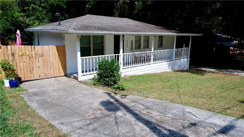 White exterior with a covered front porch featuring white railings, a paved driveway, and a wooden privacy fence