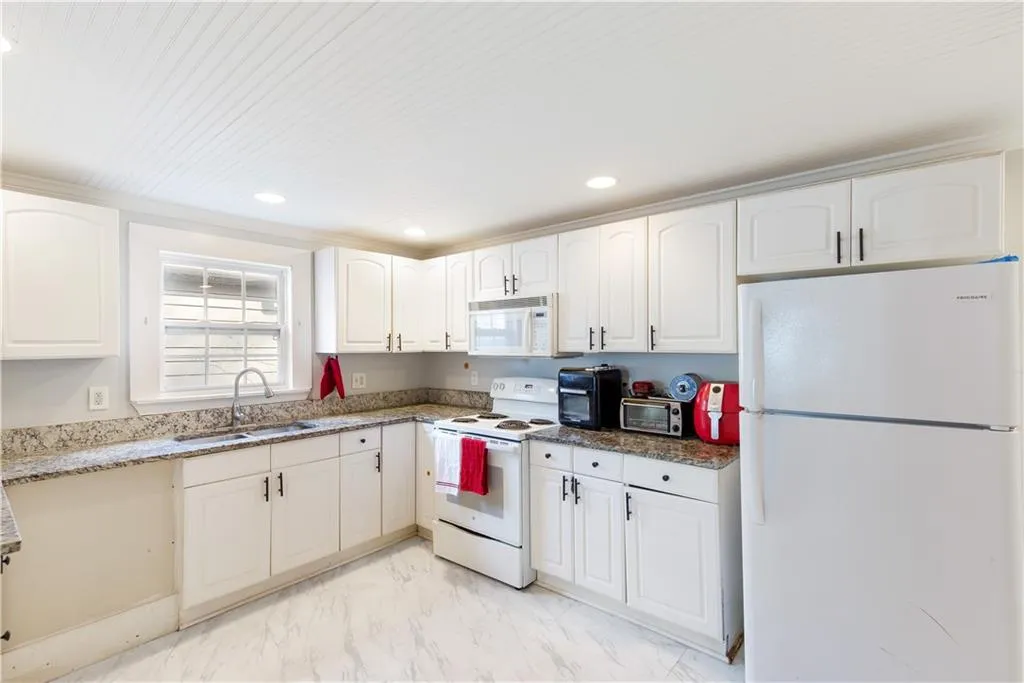 Kitchen with dark stone counters, light tile floors, white appliances, white cabinets, and sink