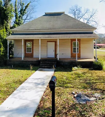 Front facade featuring a covered porch with white columns, horizontal siding, and brick-look accents