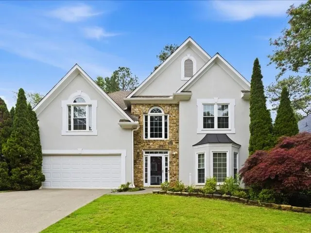 Stucco and stone facade home featuring a two-car garage, bay window, arched window details, and mature landscaping