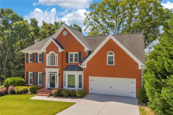 Brick colonial-style residence featuring a prominent arched window, bay window, and a two-car garage