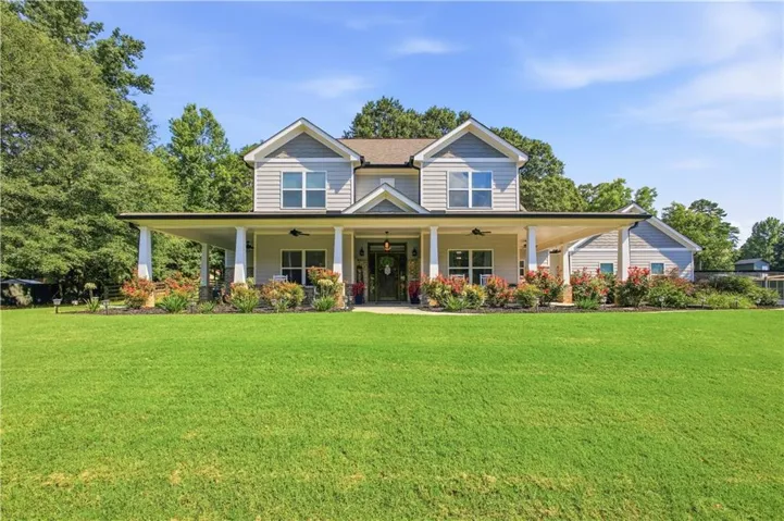 Two-story residence featuring light gray siding, a prominent covered front porch with white columns, and a landscaped front yard with mature plantings