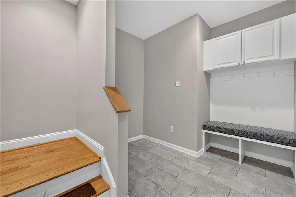 Built-in mudroom bench with upper cabinetry, coat hooks, and textured cushion